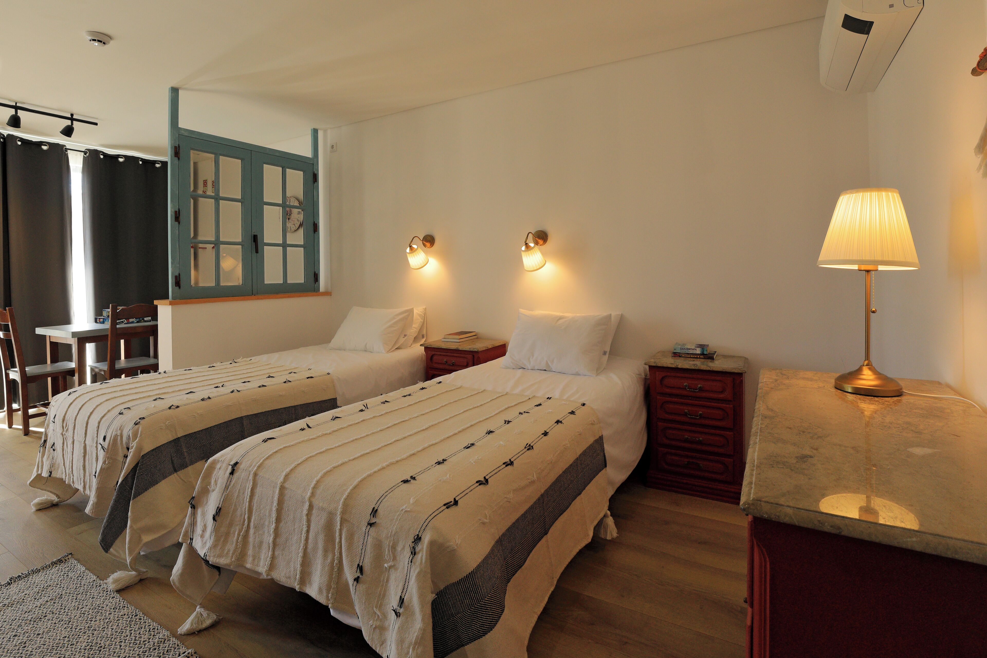 A hotel room with two beds, a desk, a chair, a nightstand, and a lamp.