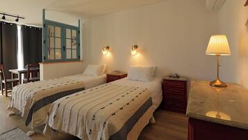 A hotel room with two beds, a desk, a chair, a nightstand, and a lamp.