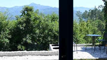 A patio area with a table and chairs, surrounded by trees and a view of distant mountains.