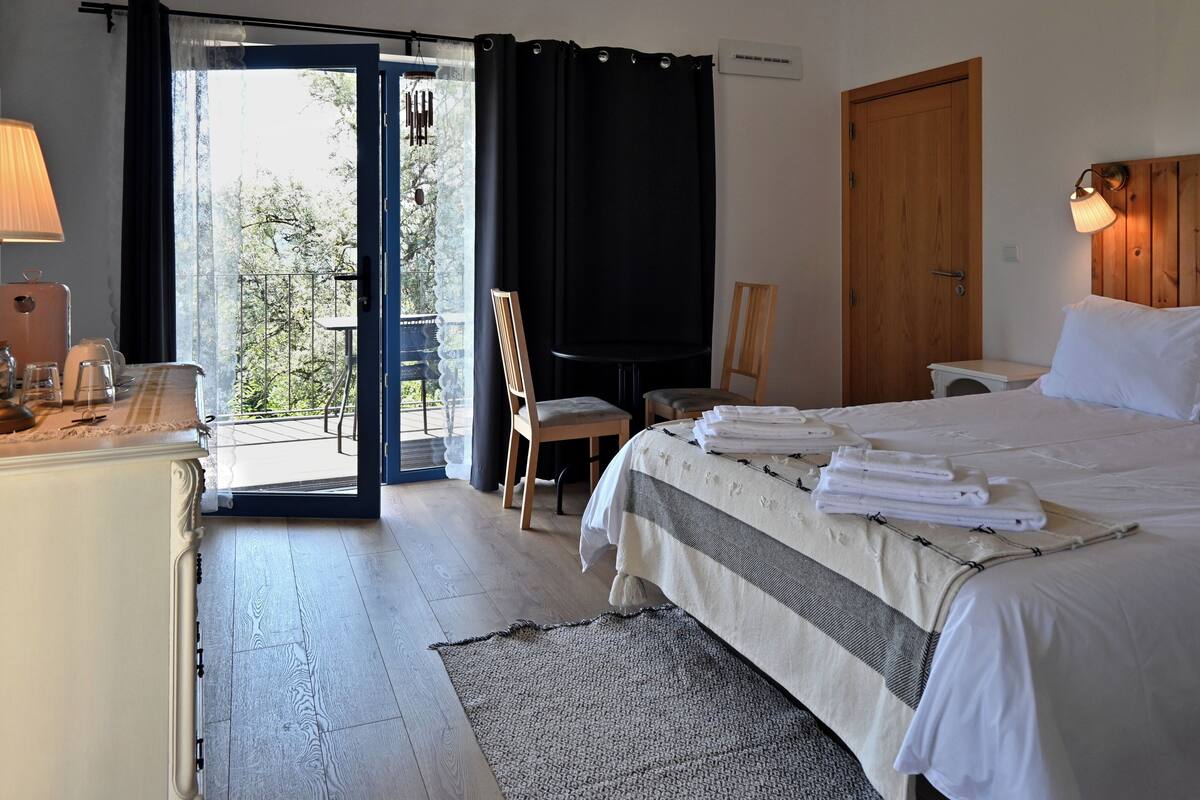 Ein Hotelzimmer mit Bett, Schreibtisch, Stuhl, Tisch und Blick ins Freie.