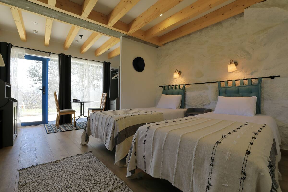 Ein Schlafzimmer mit zwei Betten, Holzbalken, einer Steinwand und Blick durch eine Tür.