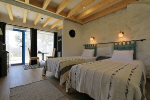 A bedroom with two beds, wooden beams, a stone wall, and a view through a door. - Peneda ecofarm (Arcos de Valdevez)