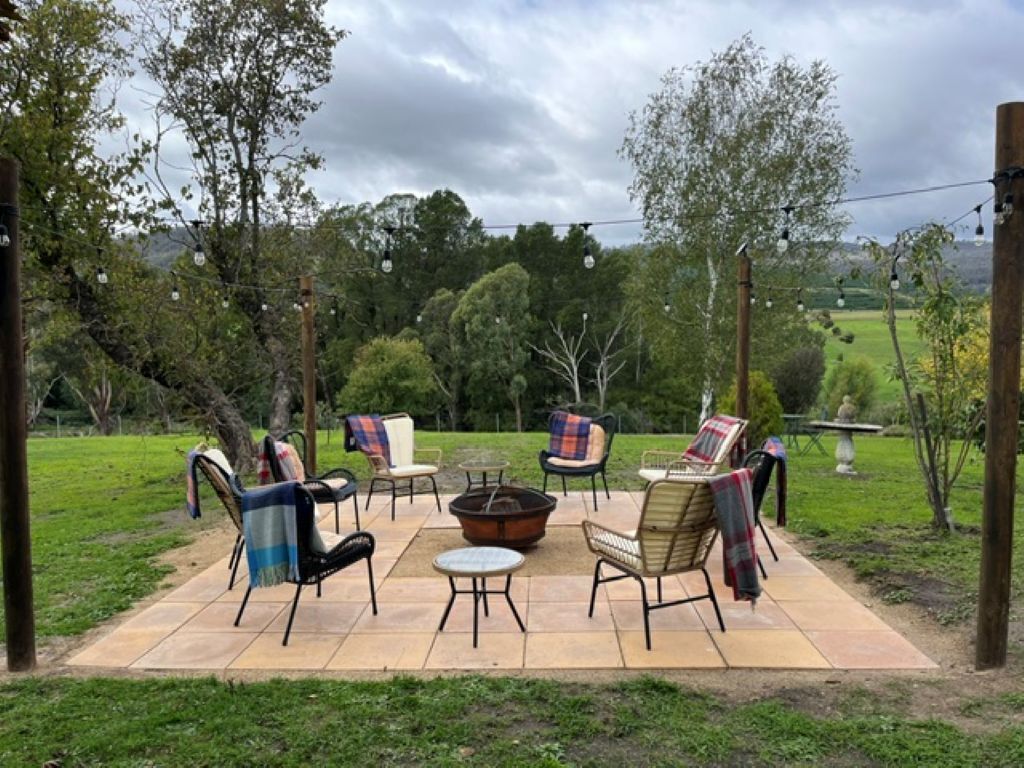 An outdoor patio with chairs and a fire pit, surrounded by a grassy area and trees.