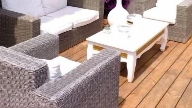 Un patio con mobiliario de mimbre, una mesa baja blanca y flores de buganvilla moradas.