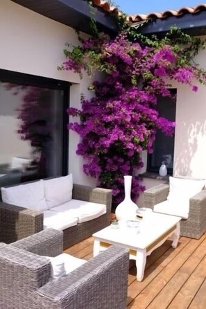 A patio with wicker furniture, a white coffee table, and purple bougainvillea flowers. - Maison Neuve Face à la Réserve Naturelle du Bagnas (Marseillan)