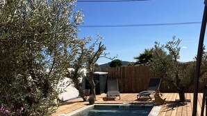 Una terraza de madera con piscina, sillones de descanso y olivos.