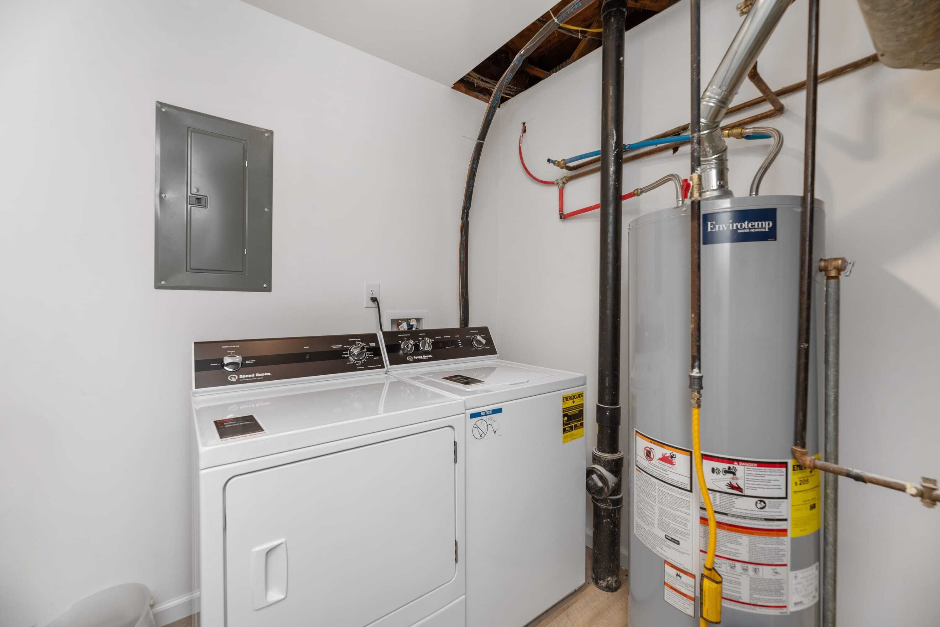 Een wasruimte met een voorlader wasmachine en droger, een boiler, en openliggende leidingen.