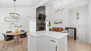 A modern kitchen with a central island, dining table, and chairs. There is a TV mounted on the wall, a fireplace, and a hanging light fixture. - Beautiful 6 bed, 3 bath home in quiet neighborhood (Wichita)