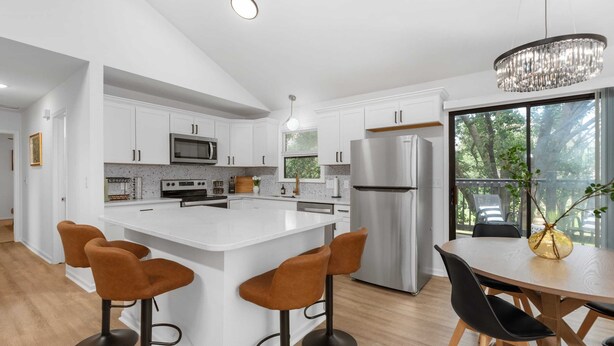 A modern kitchen with white cabinetry, a central island with bar stools, stainless steel appliances, and a chandelier. - Beautiful 6 bed, 3 bath home in quiet neighborhood (Wichita)