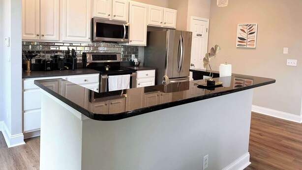 A modern kitchen with white cabinets, stainless steel appliances, and a black granite countertop.