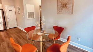 A dining area with a glass table, orange chairs, and pendant lighting.