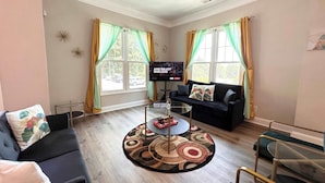 A living room with a sofa, a coffee table, a TV, and two windows with curtains.