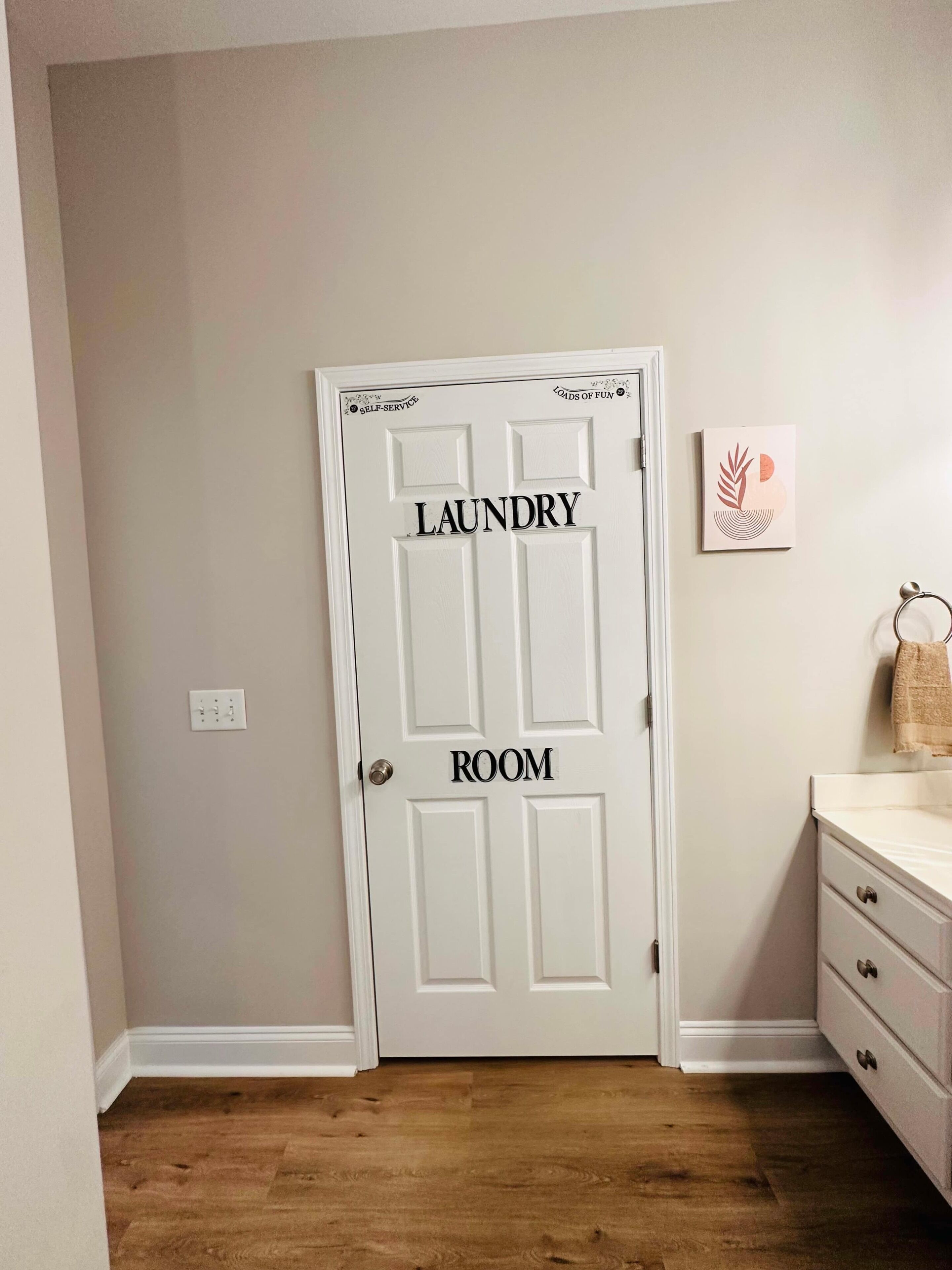 Una puerta blanca con la señalización 'LAUNDRY ROOM', un aparador blanco y un perchero con una toalla.