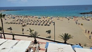 Une plage bordée de nombreux parasols et de chaises longues, une mer d’un bleu limpide et, au loin, une digue rocheuse.