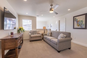 A living room with a sofa, a coffee table, a TV mounted on the wall, and a ceiling fan. - 5 BR - Siena Hills Resort - Patio, BBQ & Games (Washington)