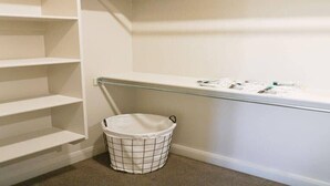 A clean, organized closet with open shelves and a hanging rod, a laundry basket, and a small trash bin. - 5 BR - Siena Hills Resort - Patio, BBQ & Games (Washington)