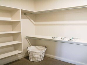 A clean, organized closet with open shelves and a hanging rod, a laundry basket, and a small trash bin.