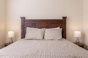A neatly made bed with a wooden headboard, two bedside lamps, and a patterned bedspread.
