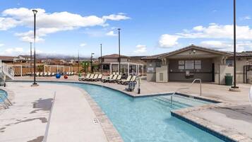 Ein Swimmingpool mit Liegestühlen und einer überdachten Liegefläche, umgeben von Gebäuden und einem klaren Himmel.