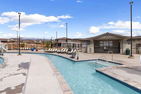 A swimming pool with lounge chairs and a covered area, surrounded by buildings and a clear sky.