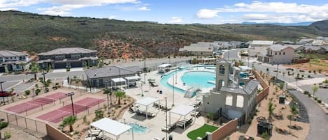 Un resort con piscina, canchas de tenis y una zona ajardinada con sillones de descanso.