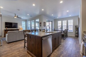 A spacious kitchen with a central island, dining area, and a living room with a sofa and TV.
