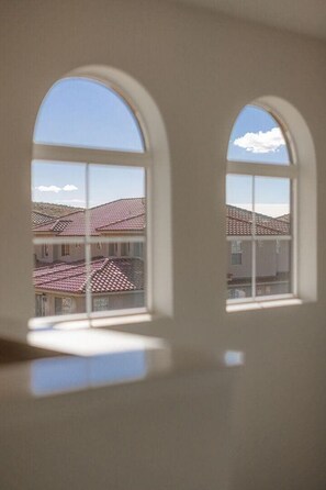 A room with two arched windows overlooking a residential area with tiled roofs.