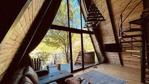 Ein gemütliches Interieur mit Holzbalkendecke, einer Couch, einem Couchtisch und einem großen Fenster mit Blick ins Freie.