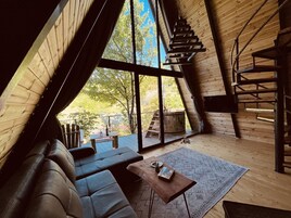 Un interior acogedor con techo de madera, un sofá, una mesa de centro y un ventanal con vistas al exterior.