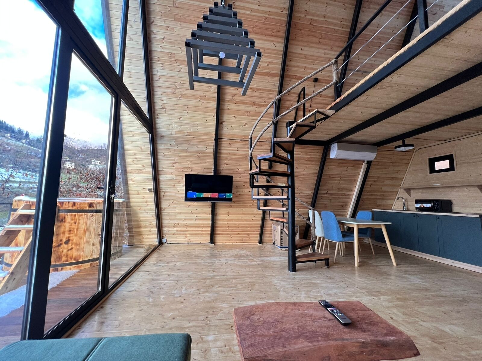 Un interior moderno con piso de madera, un televisor en la pared, una escalera y vistas al exterior.