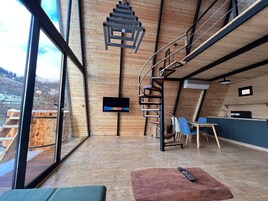 Un interior moderno con piso de madera, un televisor en la pared, una escalera y vistas al exterior.