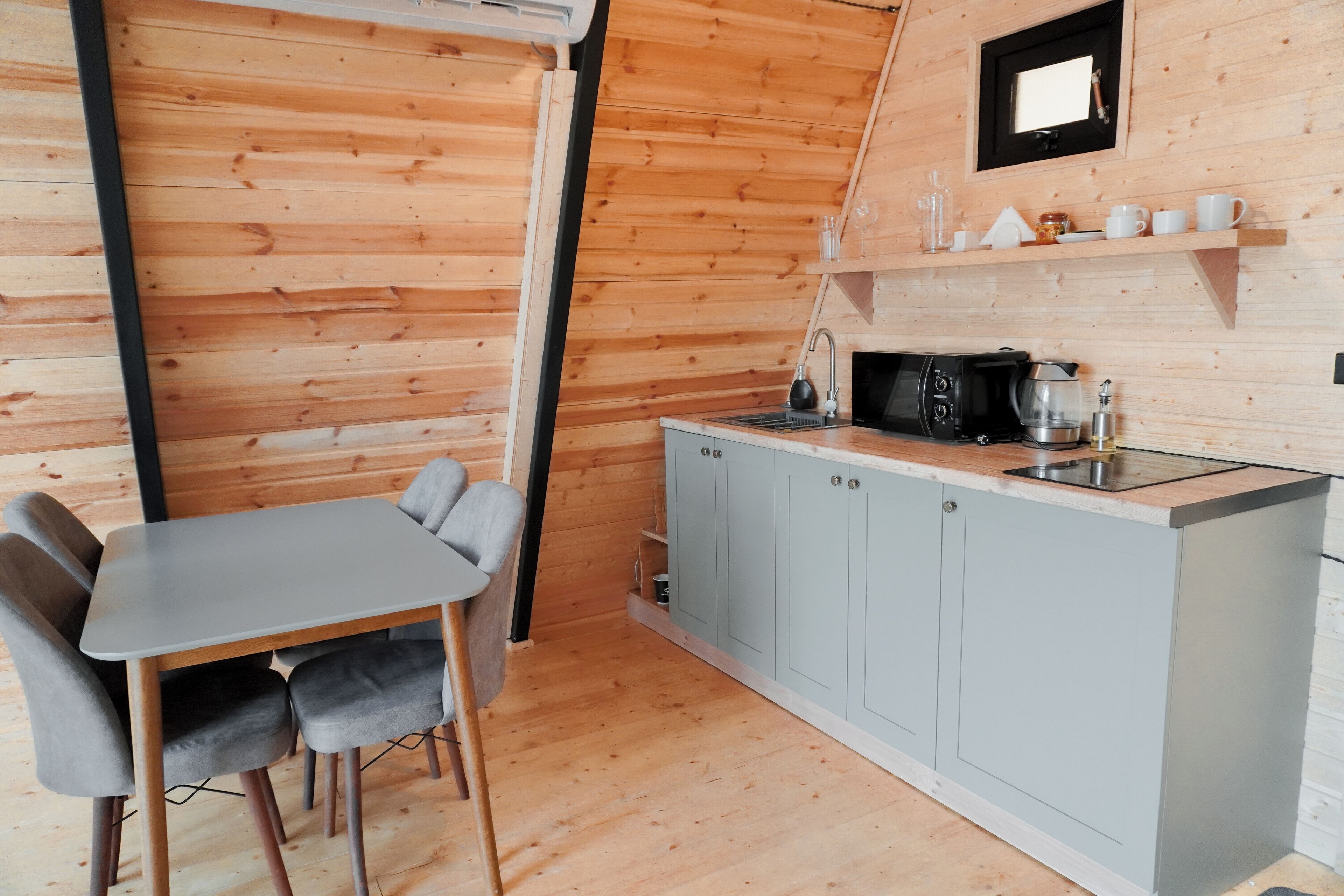 A compact kitchen with a dining area, wooden walls, and a small shelf with cups and glasses.