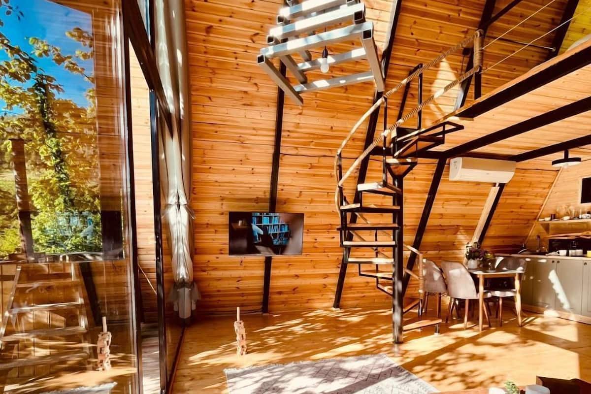 Una habitación moderna estilo loft con interior de madera, una escalera espiral y un ventanal con vistas a un bosque.