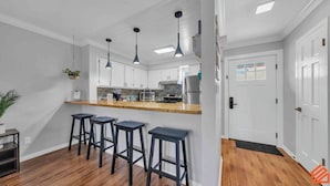 Una cocina moderna con armarios blancos, encimera de madera y tres taburetes negros.