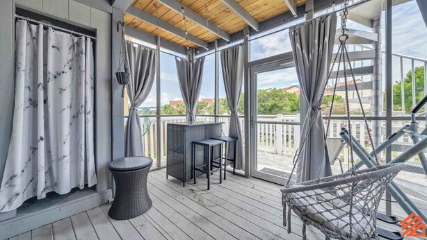 Un espacio al aire libre cubierto con una terraza de madera, dos mesas de mimbre, una silla colgante y cortinas grises.