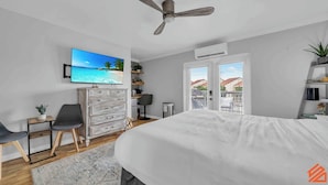 Un dormitorio con cama, televisor, escritorio, silla, cómoda y balcón con vistas.