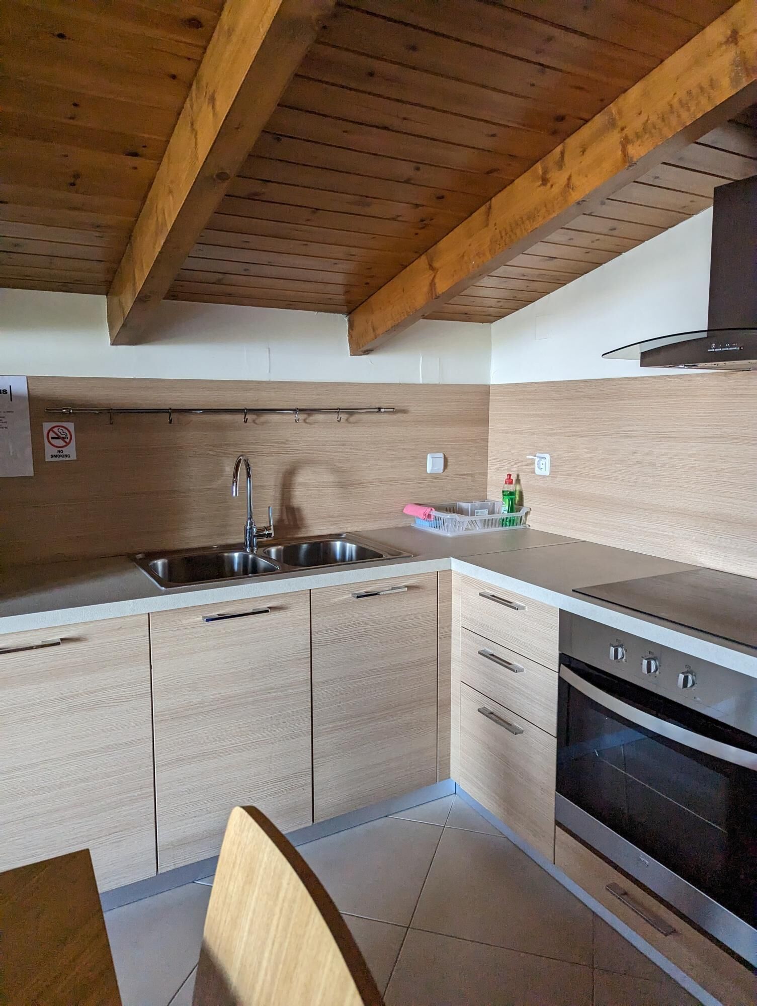 A modern kitchen with wooden beams, stainless steel appliances, and light wood cabinetry.