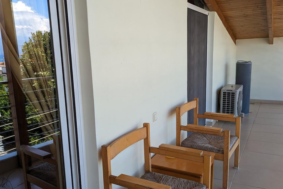 Een balkon met houten stoelen, een plafondventilator en een raam met zonwering.