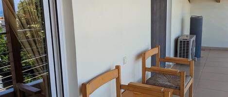 Ein Balkon mit Holzstühlen, einem Deckenventilator und einem Fenster mit Jalousien.