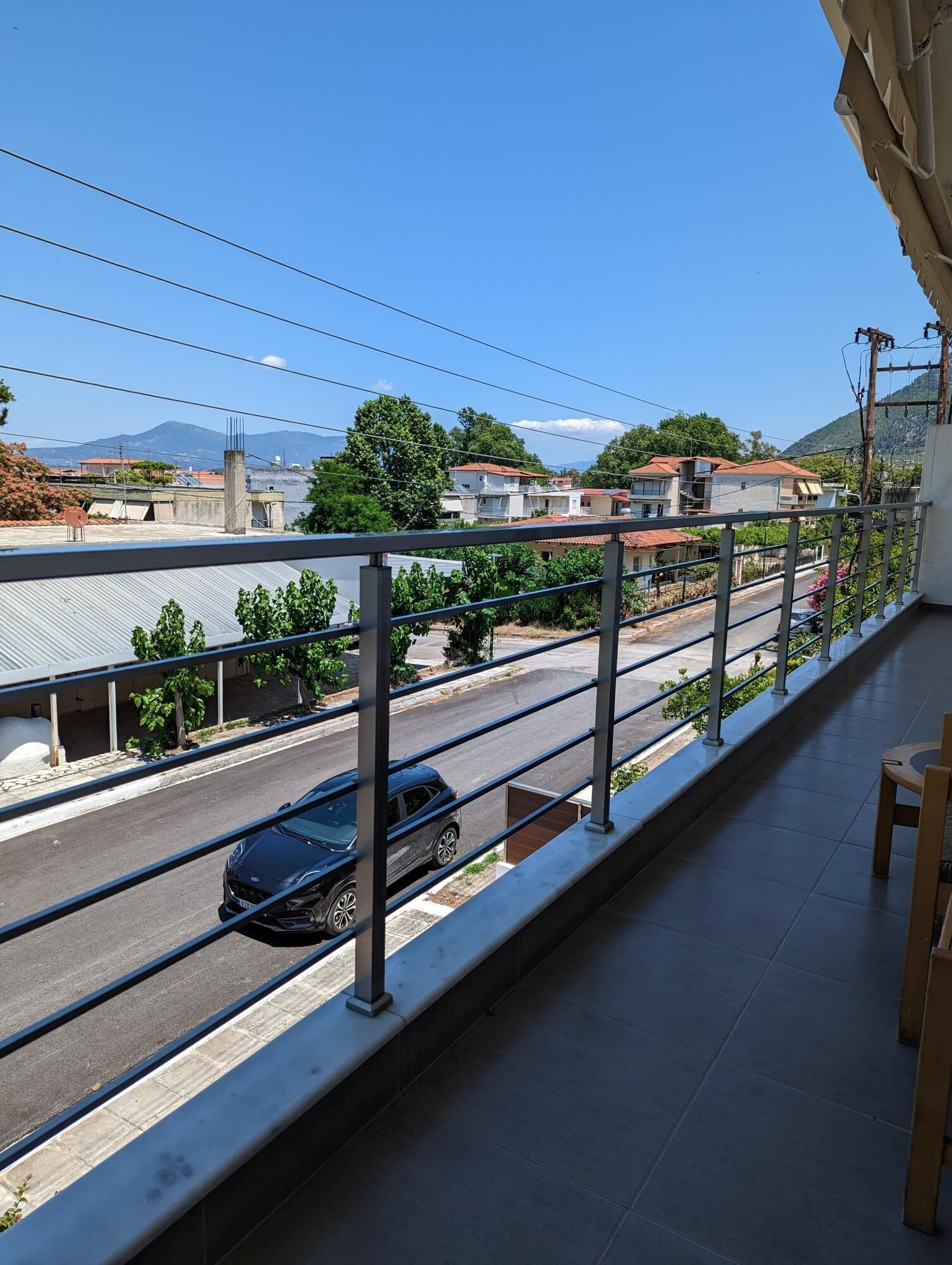 Balcón con barandilla de metal que da a una calle con un coche, edificios y una montaña al fondo.