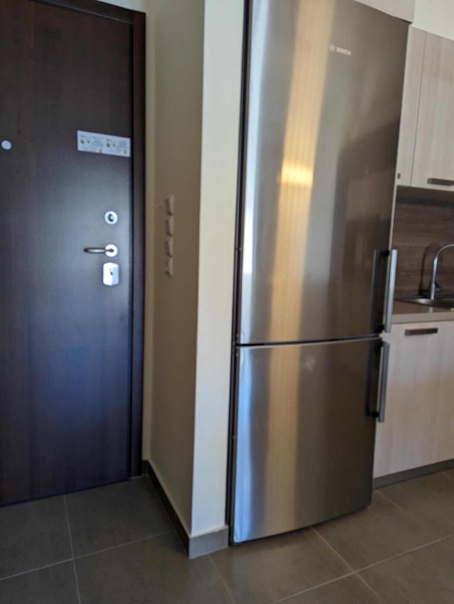 A modern kitchen with a stainless steel refrigerator, wooden cabinets, and a tiled floor.