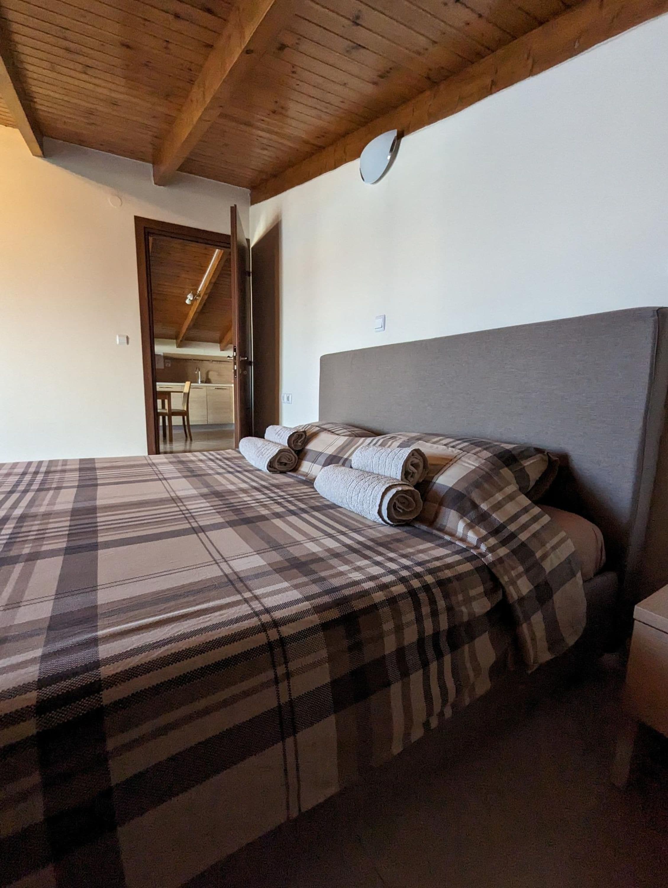 A bedroom with a wooden ceiling, a bed with plaid bedding, and a small bedside table.