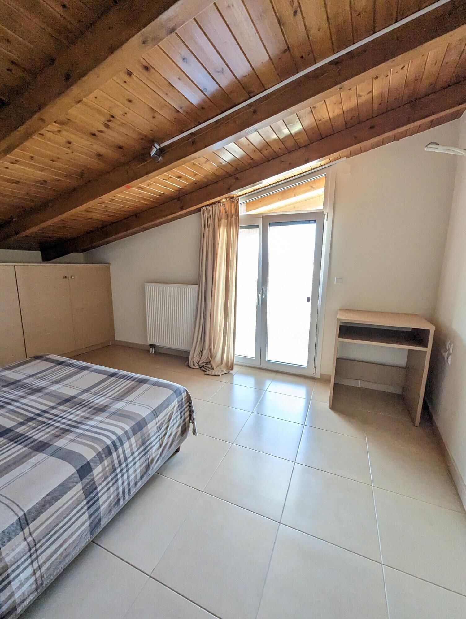 Un dormitorio con cama, escritorio, radiador y ventana con cortinas.