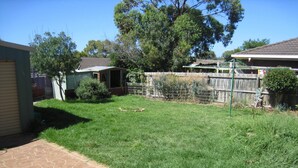 A residential backyard with a paved patio, a fenced area, and a variety of trees and shrubs. - Comfy family holiday destination (Ocean Grove)