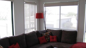 A living room with a sectional sofa, a wooden coffee table, and large windows. - Comfy family holiday destination (Ocean Grove)