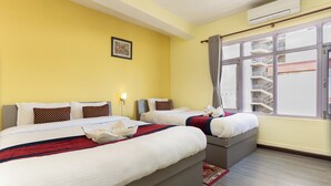 Une chambre d’hôtel avec deux lits, une fenêtre donnant sur l’immeuble et un climatiseur fixé au mur.