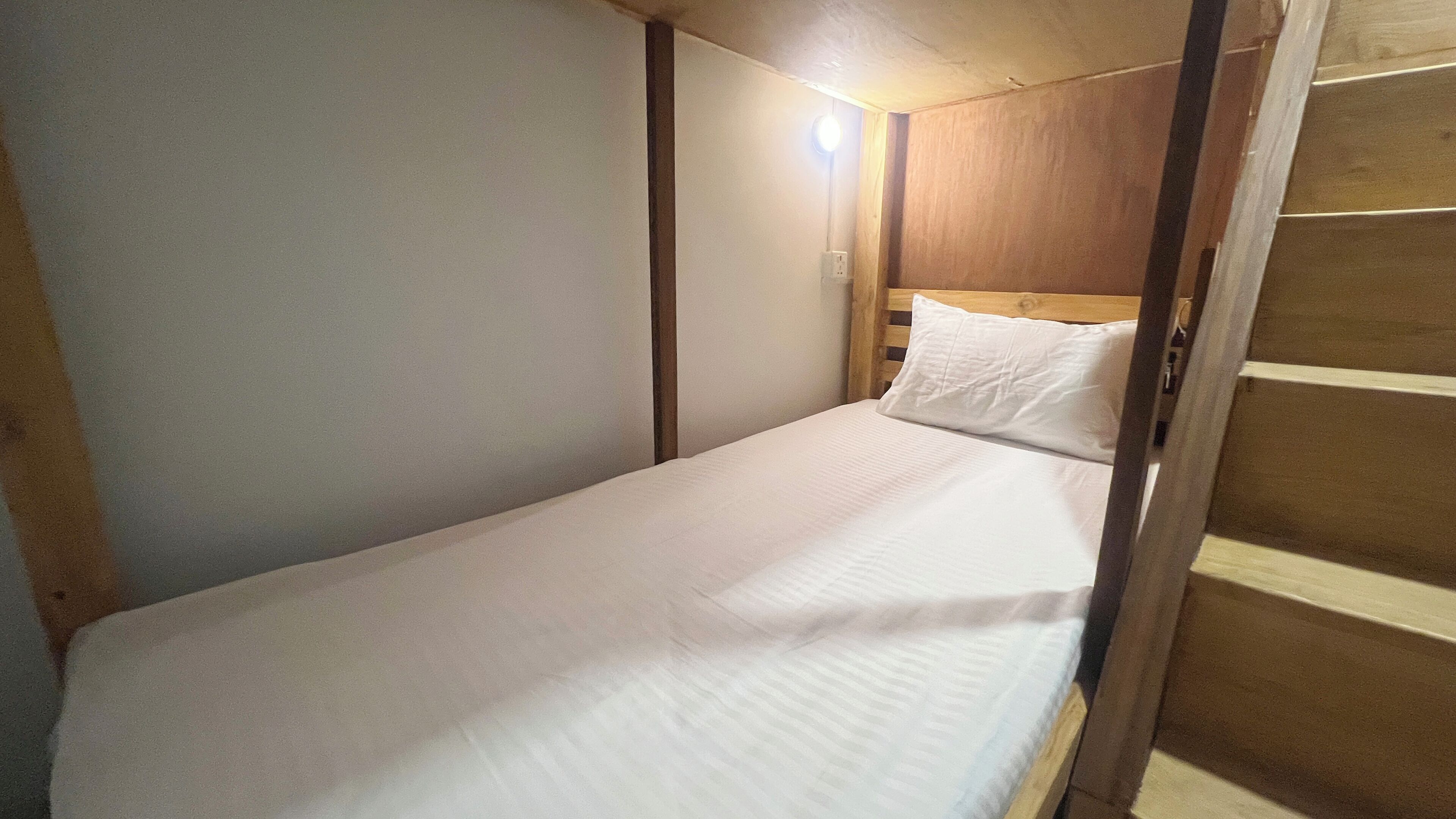 A single bed with a wooden headboard and a white mattress in a small, enclosed room with a slanted ceiling.
