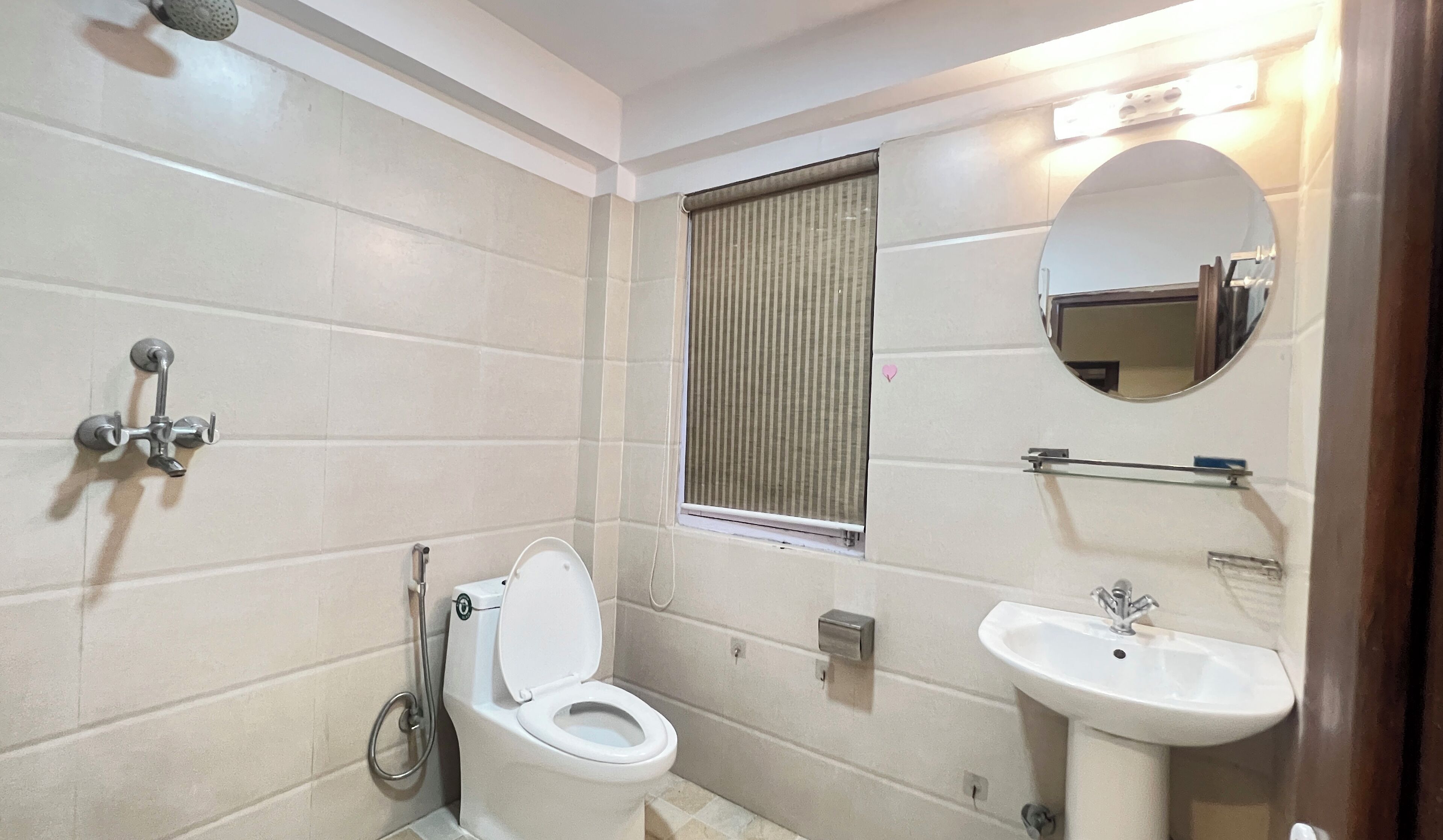 A bathroom with a toilet, sink, shower, and a window with blinds.