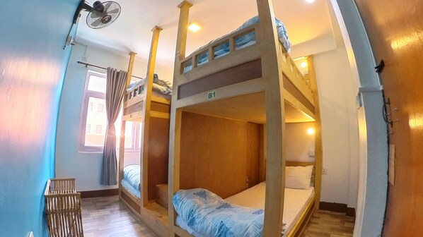 A bunk bed room with a fan, a window with curtains, and a wooden floor. - Thamel Hotel & Spa (Kathmandu)