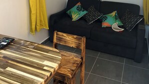 A room with a black sofa, wooden chair, and a table with a remote control.